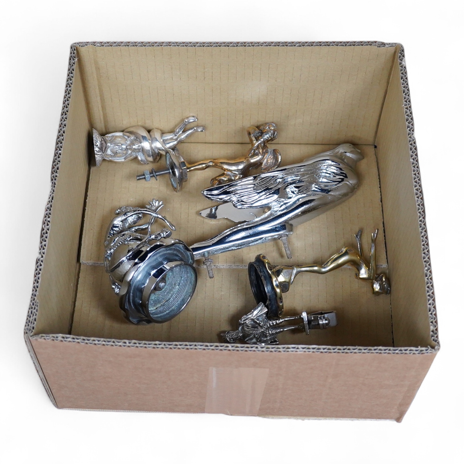 Six chrome and brass car mascots, including; a figure with a dolphin, a figure of Cupid, a grotesque in the form of a devil, a figure of a Tudor gentleman, an Art Deco figure of a flying woman, etc.